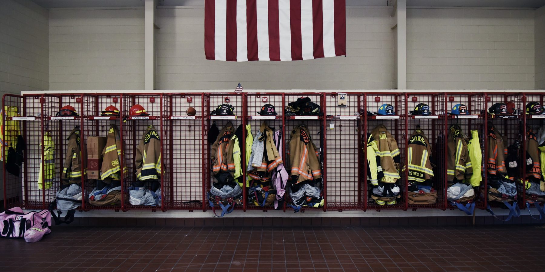 A row of turnout gear on racks in a fire station, an American flag on the wall above