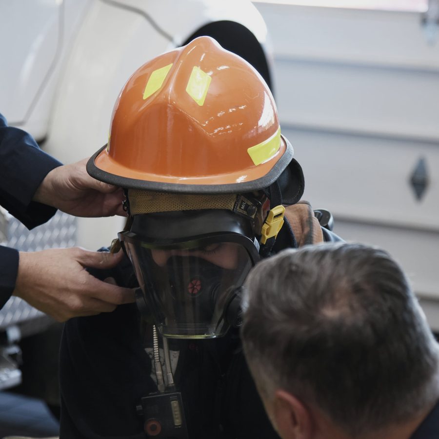 Two firefighters helping another fit a face piece
